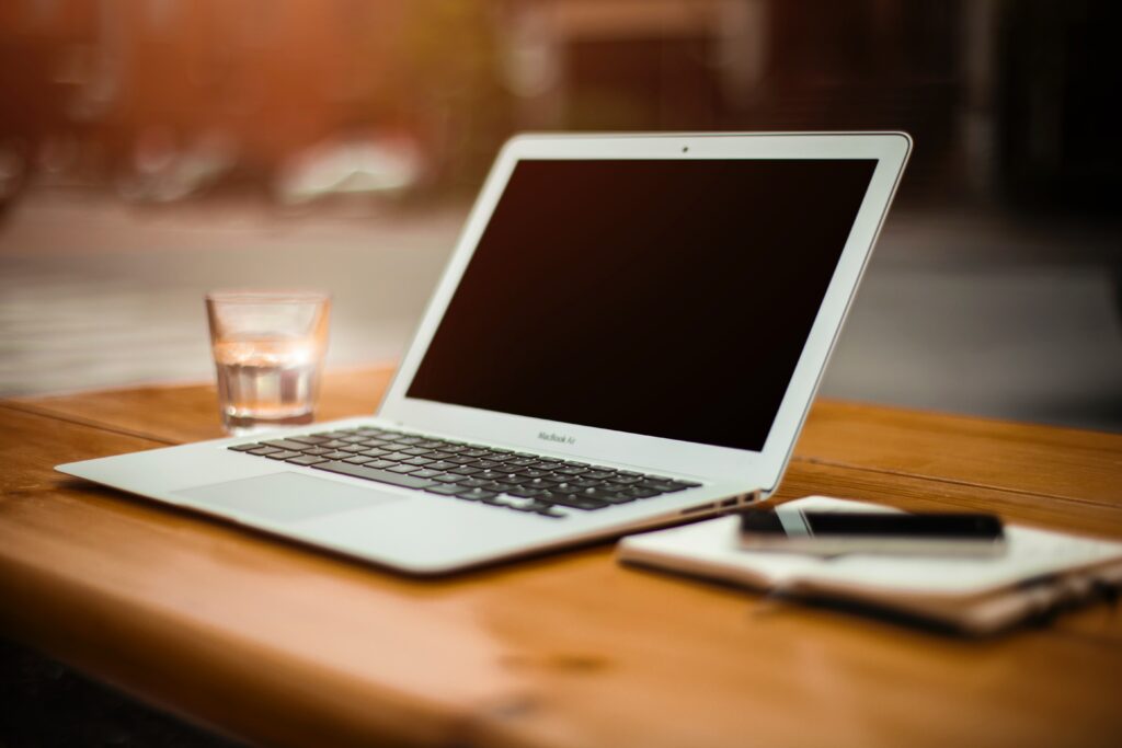 Open laptop and note pad on wooden desk.