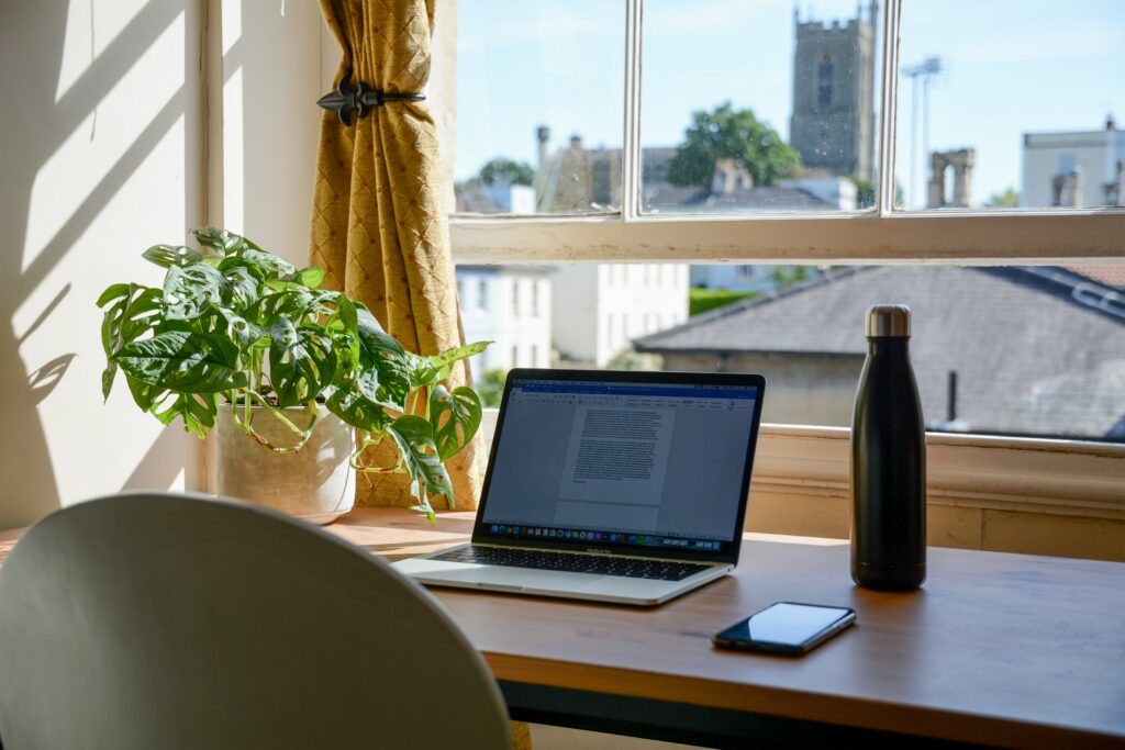 Laptop, plant and a green bottle on a desk beside an open window