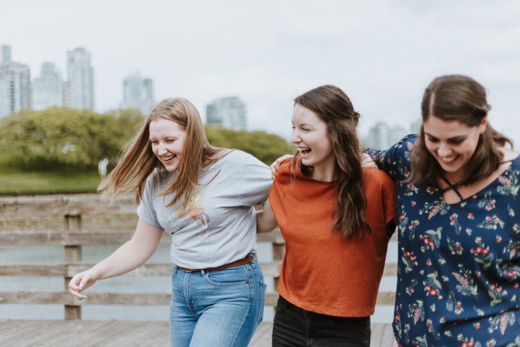 3 young people walking arm in arm, smiling and laughing together. In the background are high rise buildings.