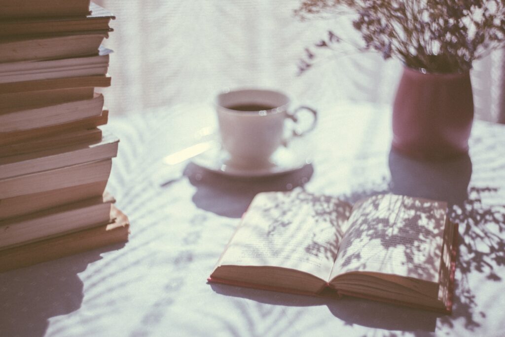 Moody image of an open book and  a cup of tea beside a sunny window.