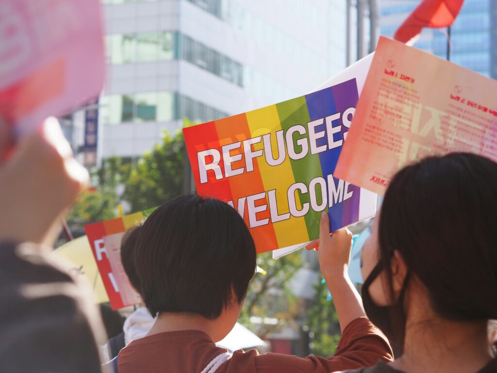 A person in a demonstration, holding a sign that says 'Refugees Welcome'