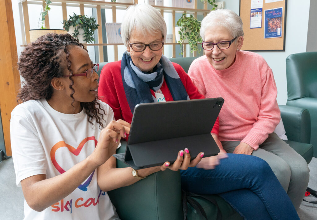 A Sky Digital Champion sharing some tips with 2 older women