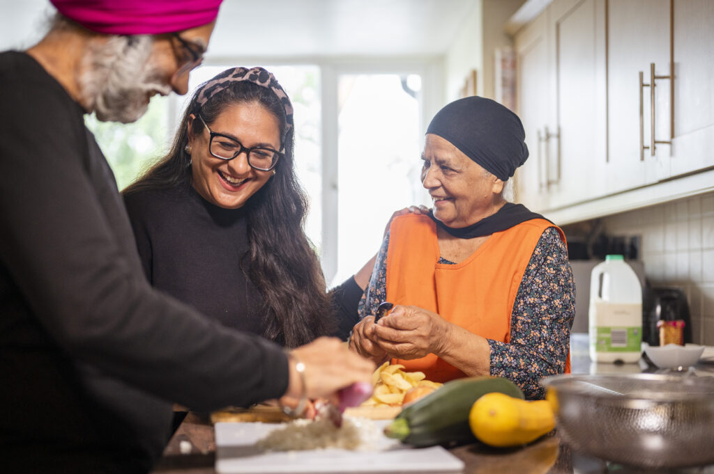 Three people happily preparing food together in a kitchen.