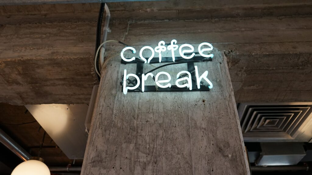 Photograph of a neon sign on a brick wall that says 'coffee break'