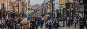 A busy pedestrianised street in Leeds. People walk closely together with buildings surrounding them on both sides. 