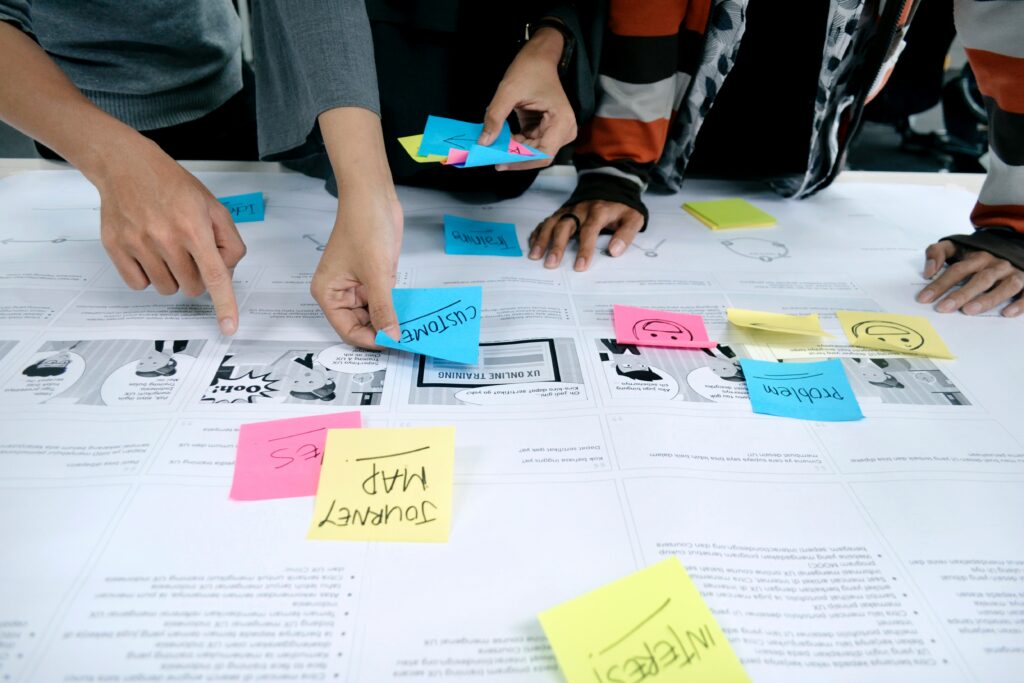 Close-up of people's hands placing colourful post-it notes with text and smiley faces on wireframes.