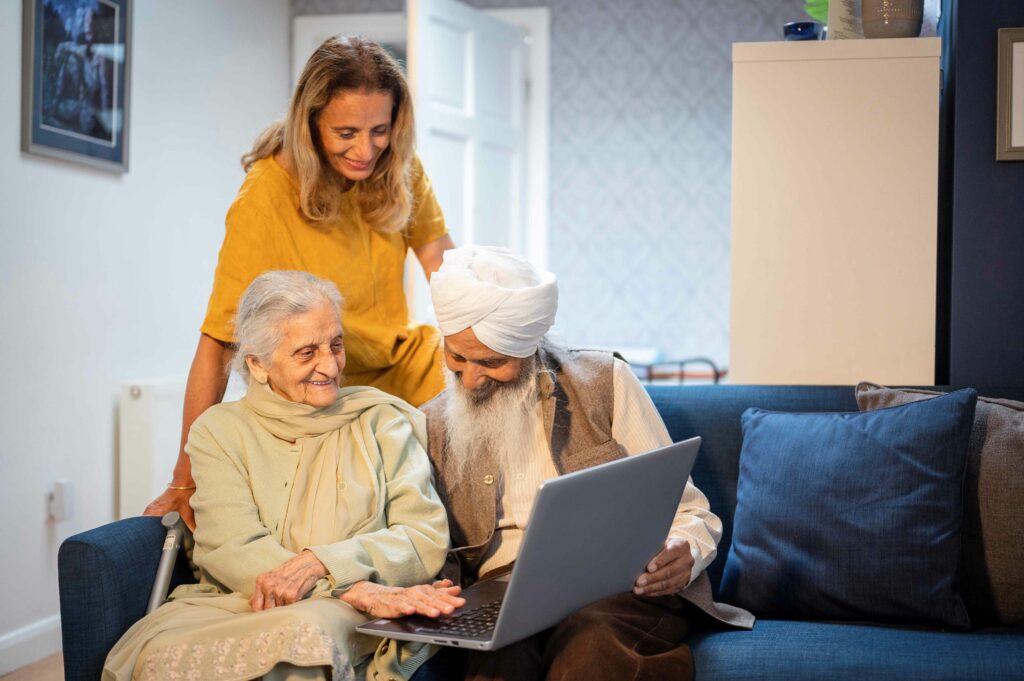 Two older people looking at a laptop, with someone standing behind them.