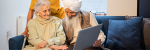 Two older people sitting on a sofa and looking at an open laptop that rests on their knees.