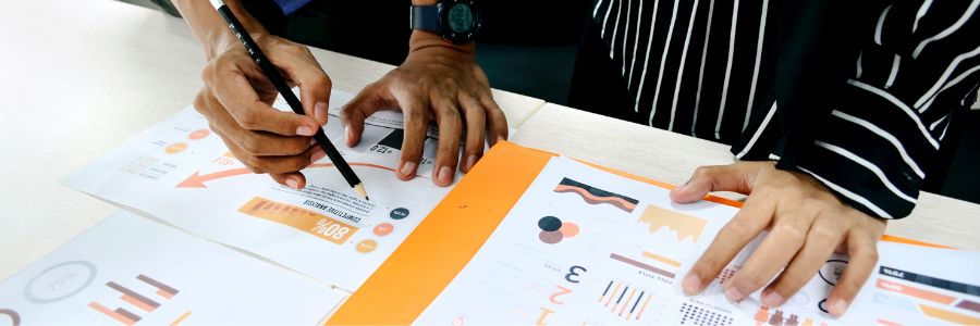Close-up of two peoples' hands and papers showing data and graphs.