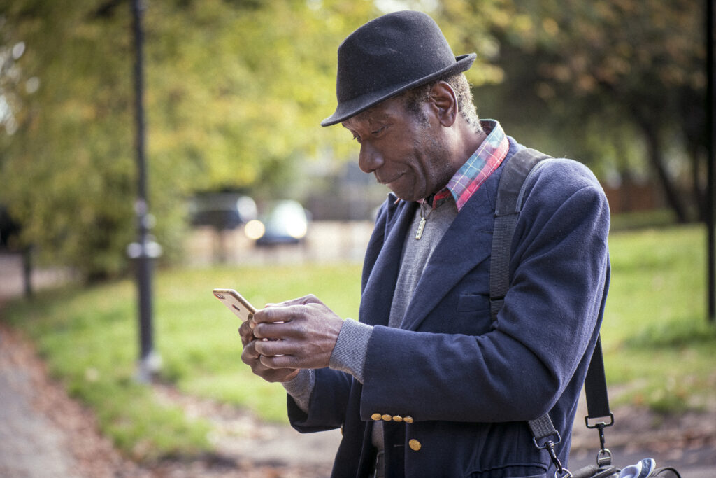 An older person smiling as he looks down at his mobile phone.