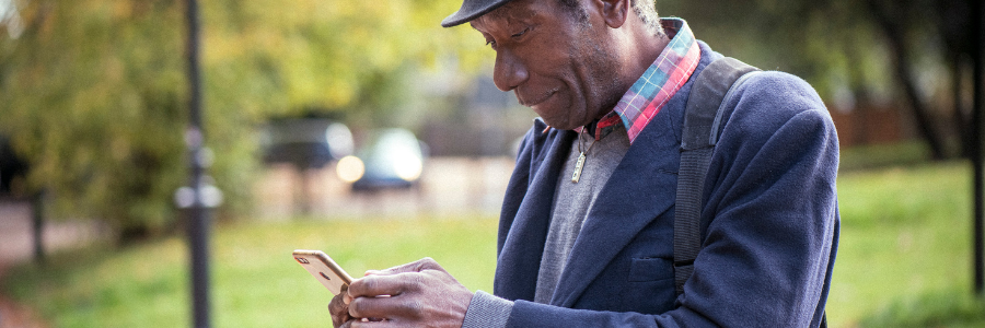 Older man smiling at he looks at his phone.