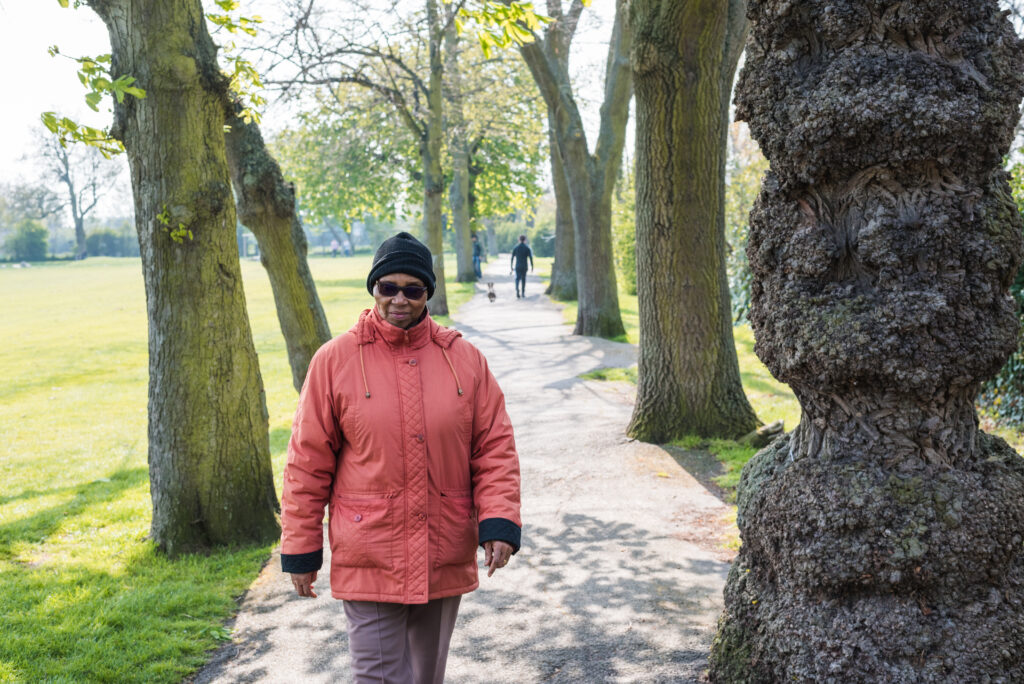 An older person walking outside along a tree-lined path.