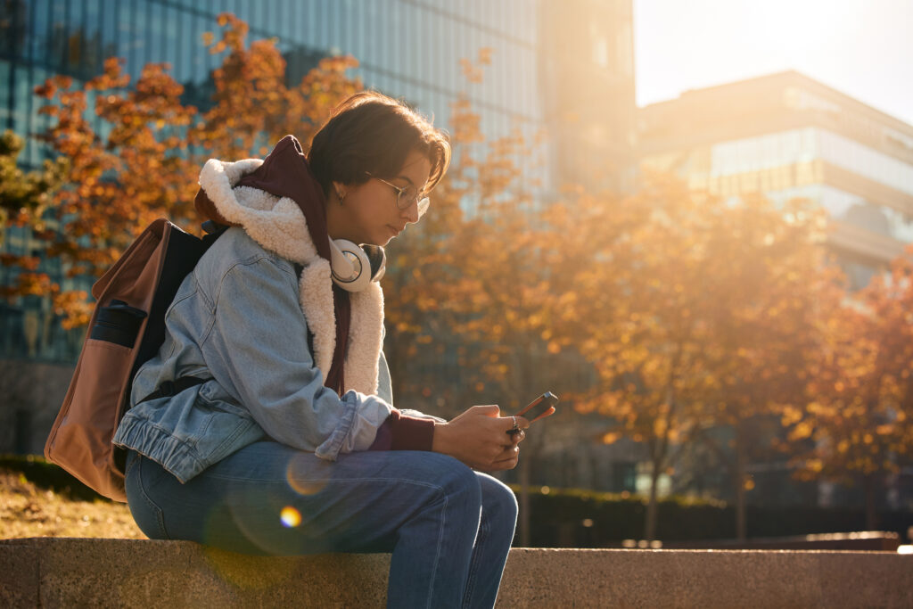 young student sits alone on a wall at a university campus surrounded by Autumnal trees