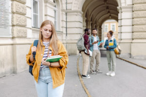 a group of students enjoying conversation, while one student is stood alone further away looking sad.