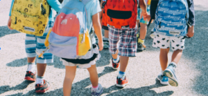 Children wearing colorful backpacks walking together on a school playground.