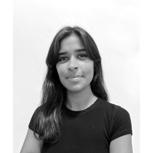 A black-and-white portrait of Isabel Doraisamy, a young woman with long straight hair, wearing a plain black t-shirt. She is looking slightly forward with a calm expression on her face, with minimal background detail.