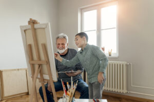 Senior man and child artist with easel, palette and paint brush painting picture at studio