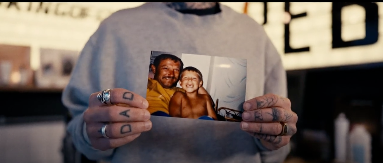 Ben's tattooed hands with the word 'dad' written across his knuckles holding a picture of him as a child with his dad.