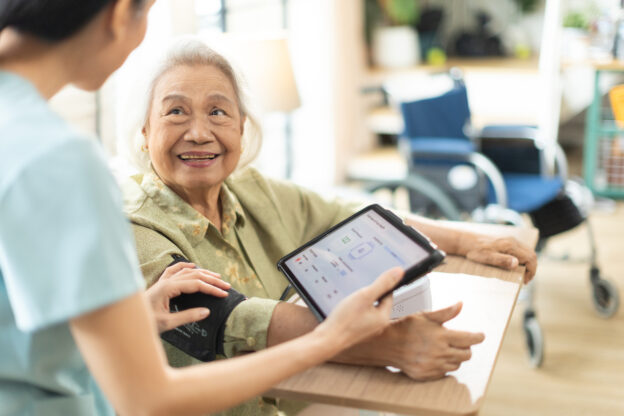nurse taking blood pressure of a senior woman patient at home.Home care healthcare professional using digital tablet
