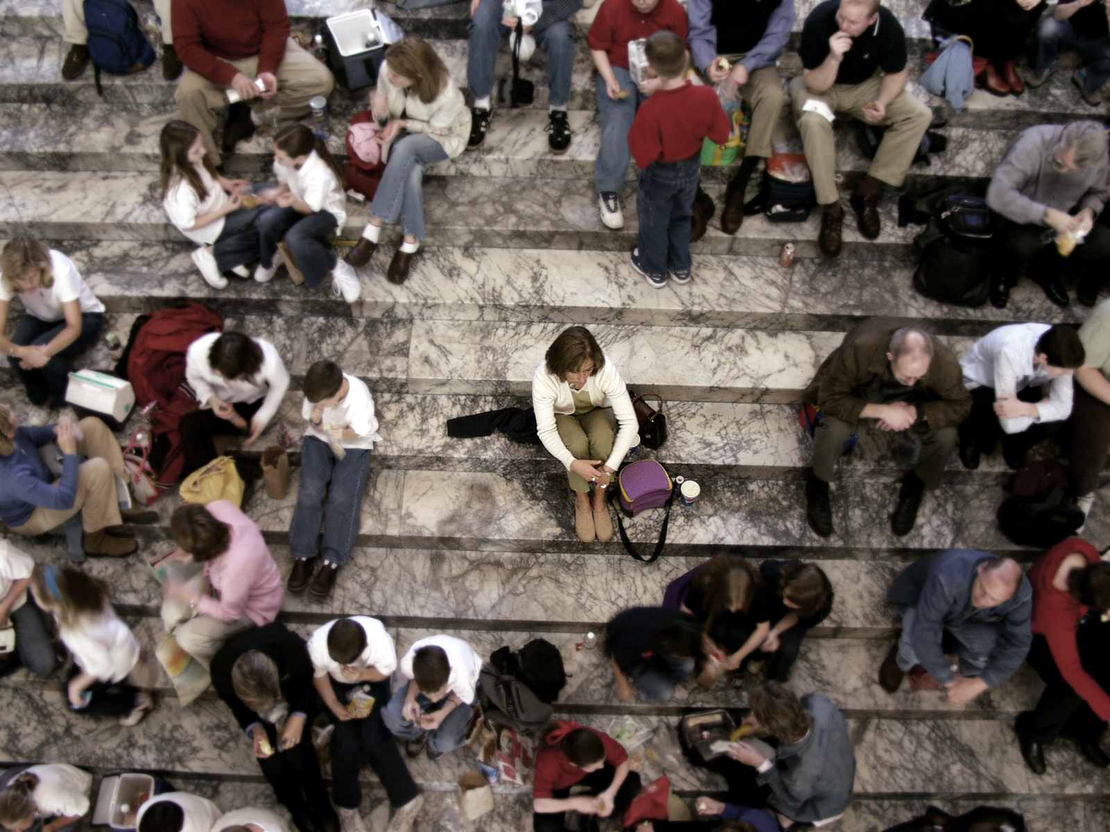 ‘An aerial view image of a person alone in a crowd. The image was intentionally softened and colours muted to all but the alone person in the middle surrounded by people.