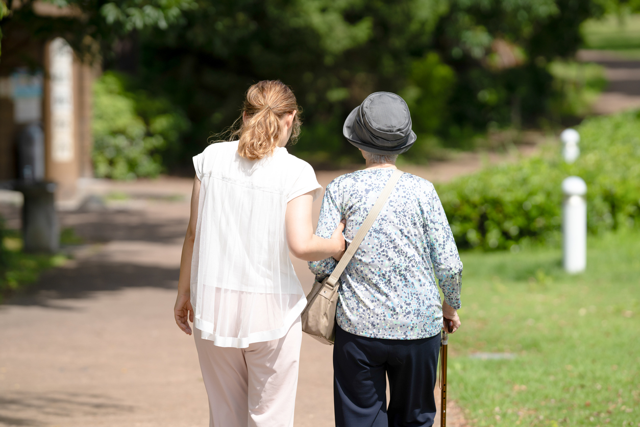 an elderly woman and her carer are walking around the park.