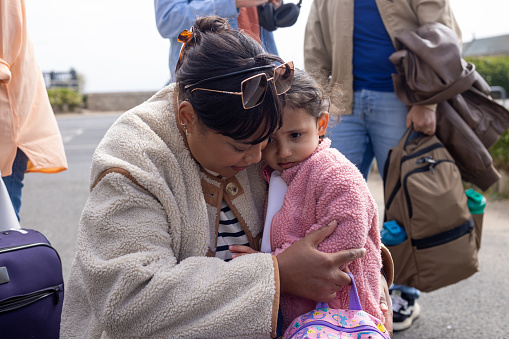 ‘Mother with her young daughter waiting to get on a coach. The girl looks upset, learning against her mother.