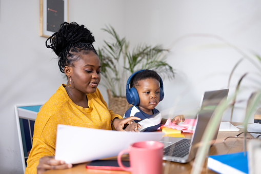 ‘Young mother managing her work tasks while caring for her baby son at home