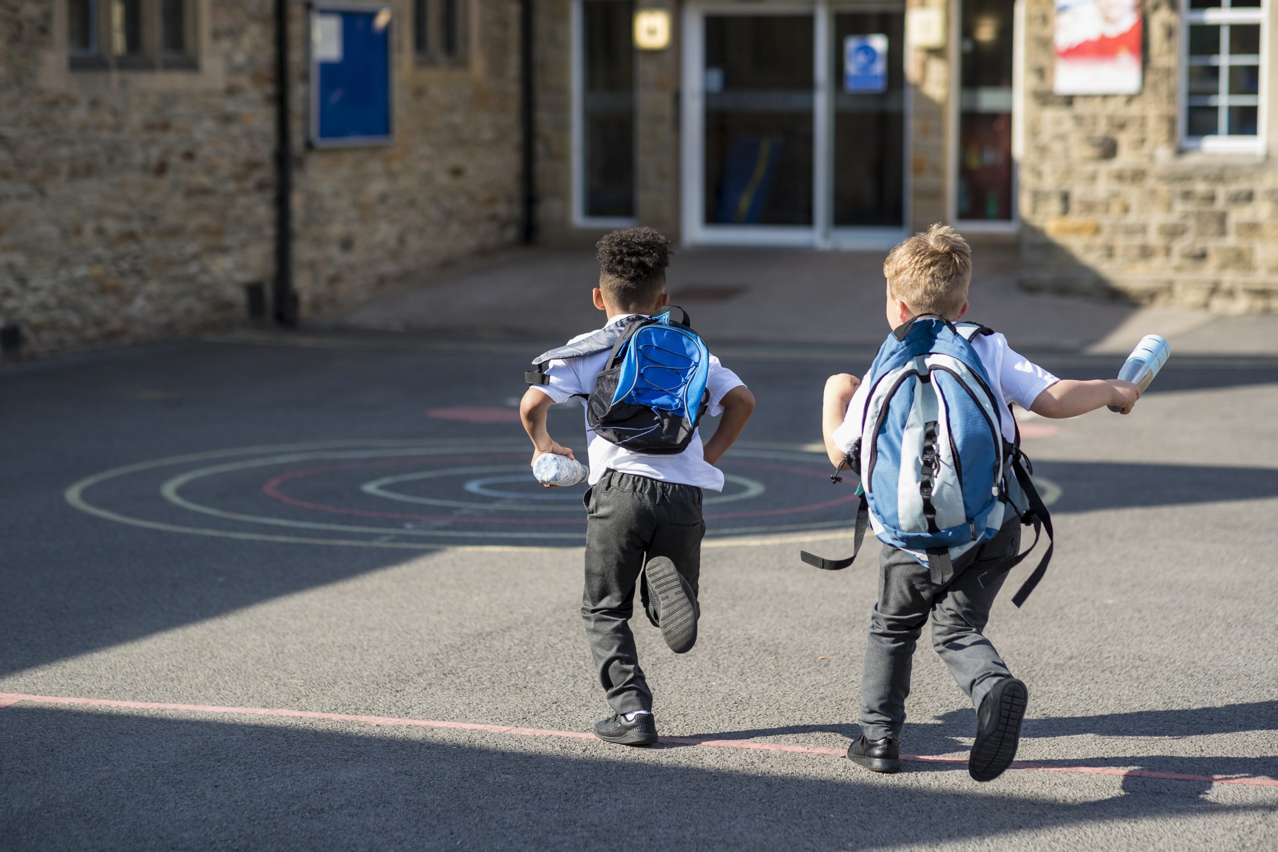 Two young children with backpacks running toward a school entrance