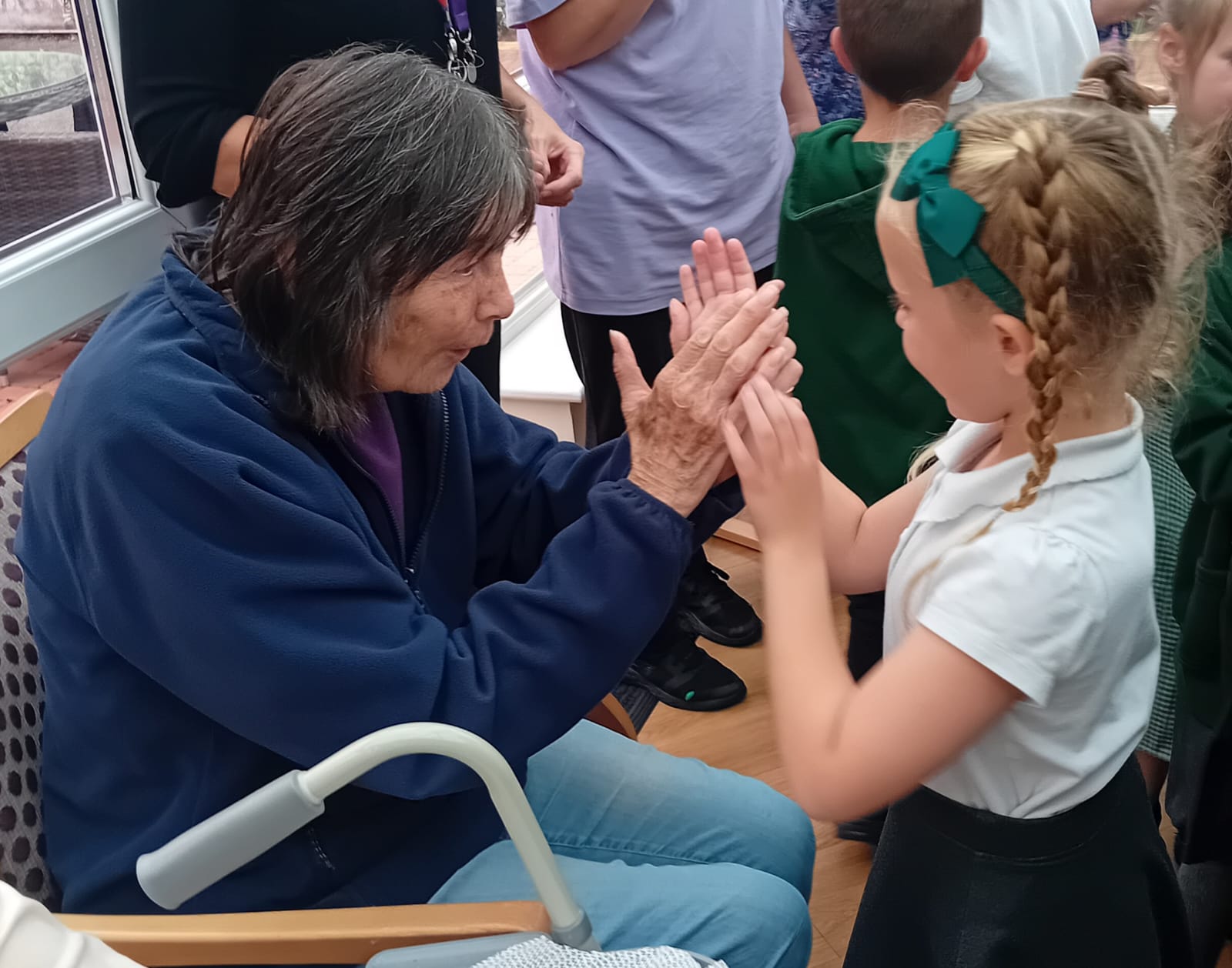 An elderly person and a young girl playing a hand-clapping game, sharing a joyful intergenerational moment.