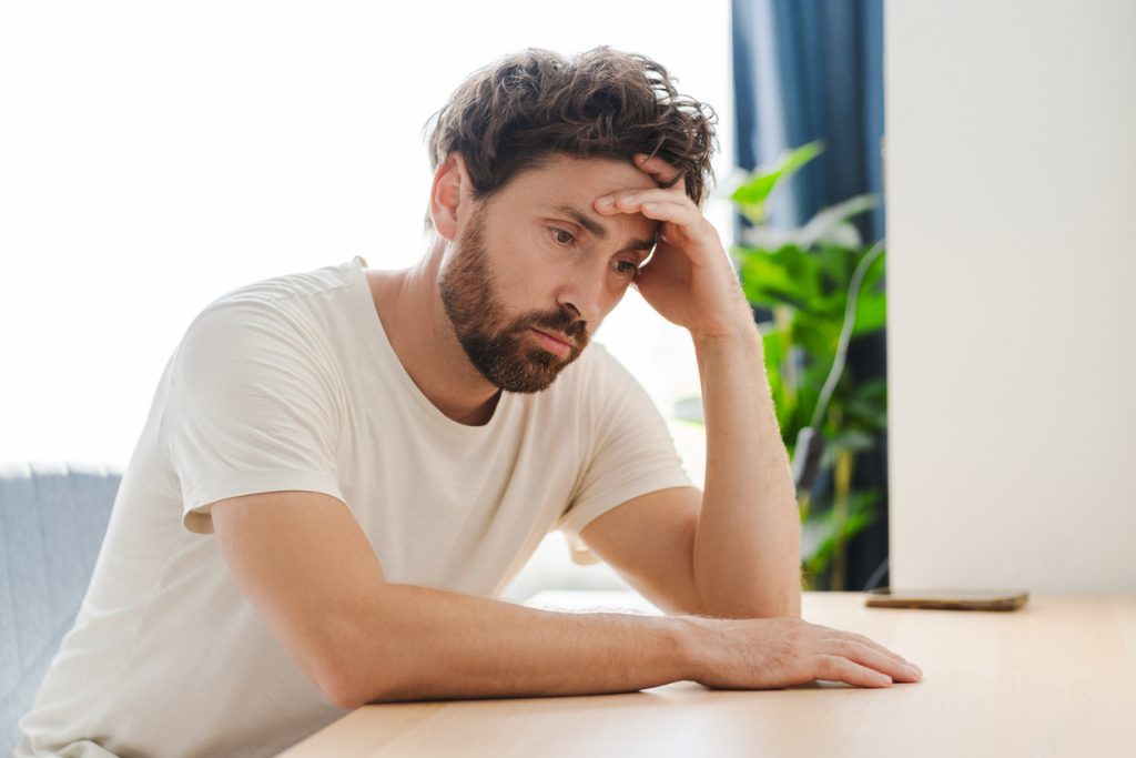 Concentrated upset young man bowing head while having headache