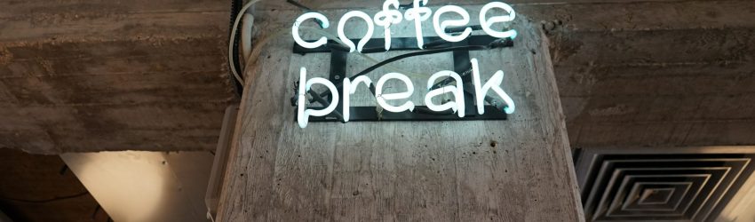 Photograph of a neon sign on a brick wall that says 'coffee break'