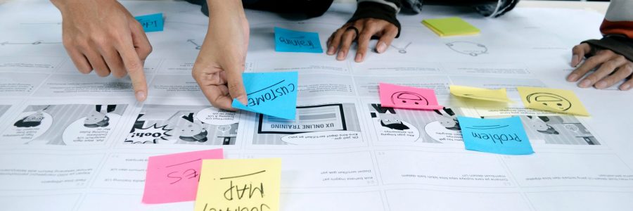 Close-up of people's hands placing colourful post-it notes with text and smiley faces on wireframes.